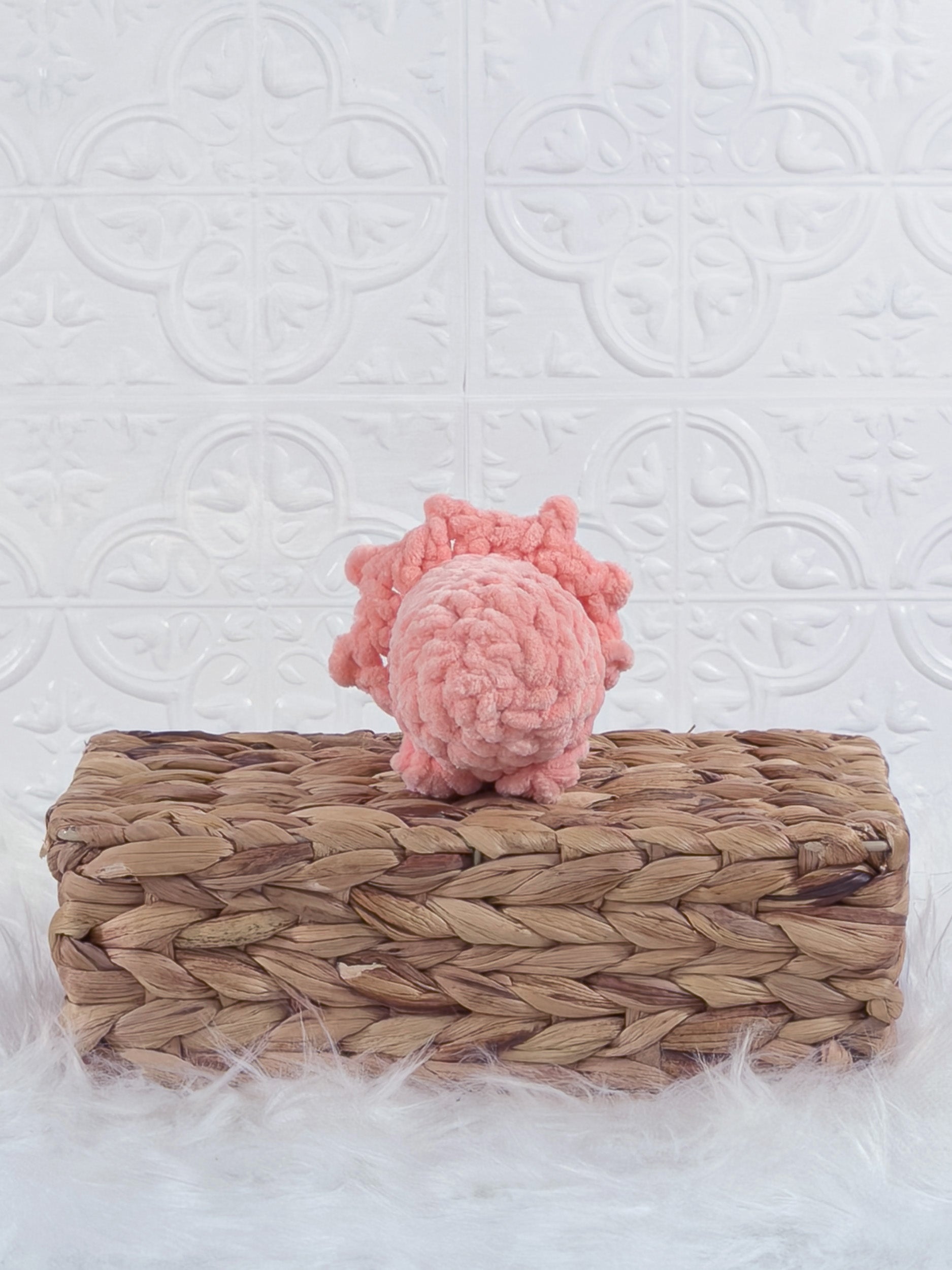 Handmade coral triceratops crochet plushie shown from the back