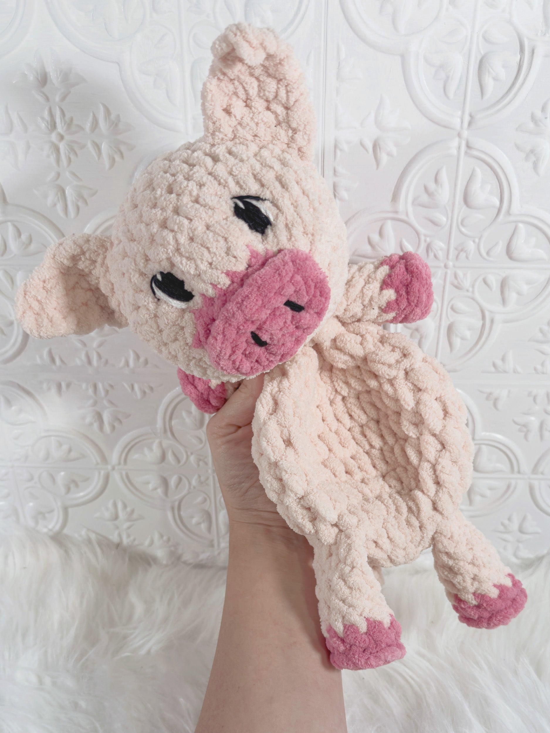 A handmade crocheted plush pig toy held in a person's hand against a white textured background.