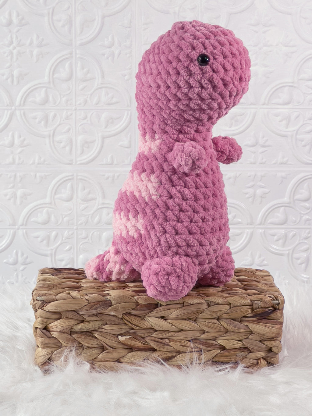 Handmade pink t rex crochet plushie shown from an angled view