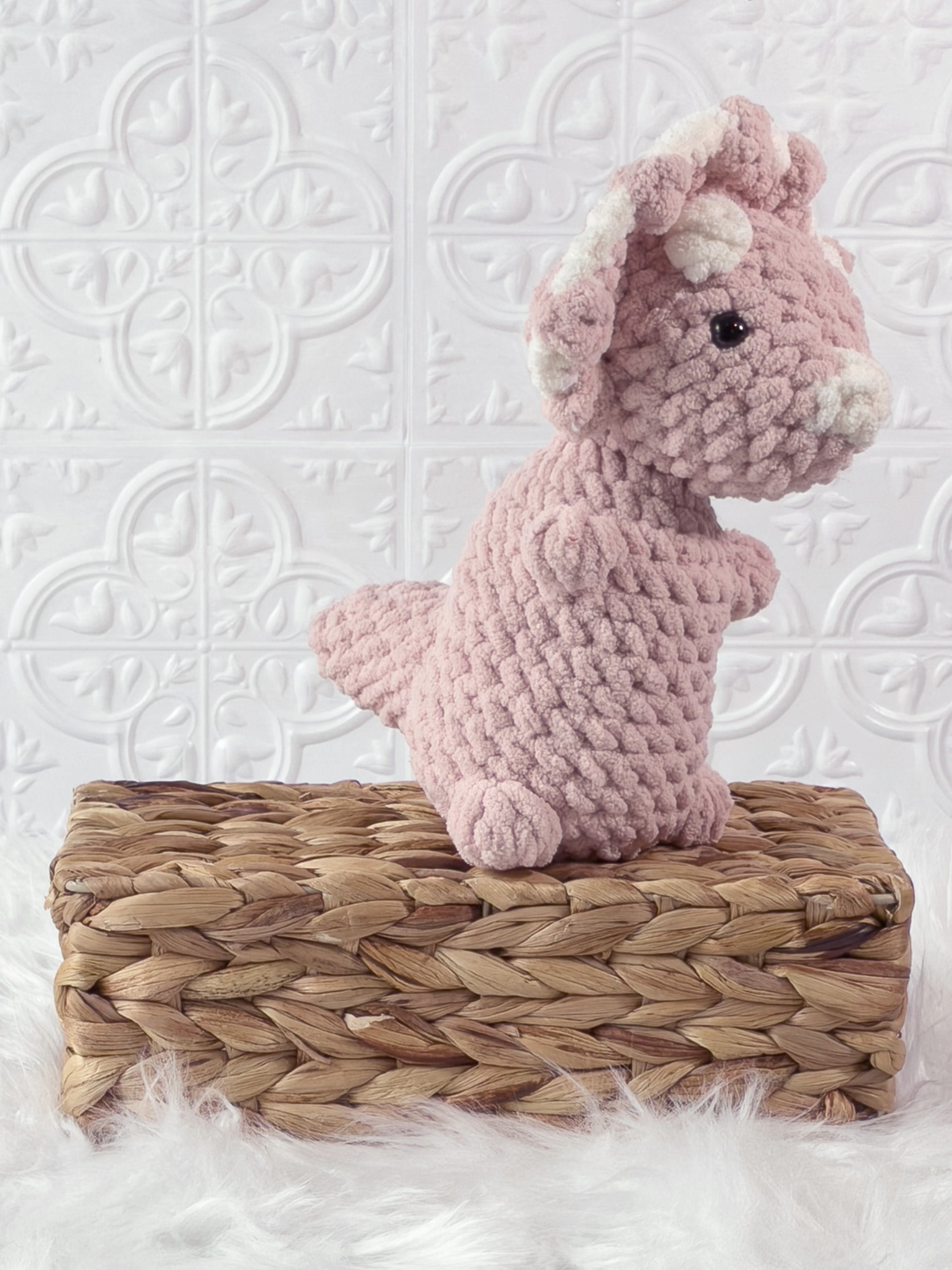 Handmade pink , light triceratops crochet plushie shown from an angled view