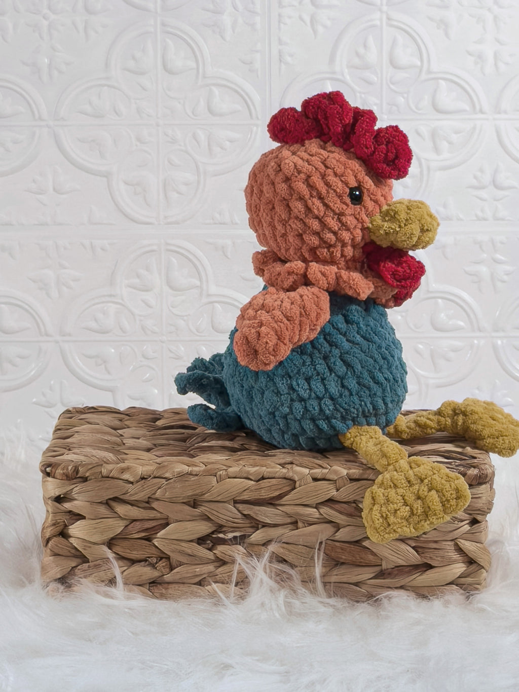 Handmade turquoise sitting rooster crochet plushie shown from an angled view